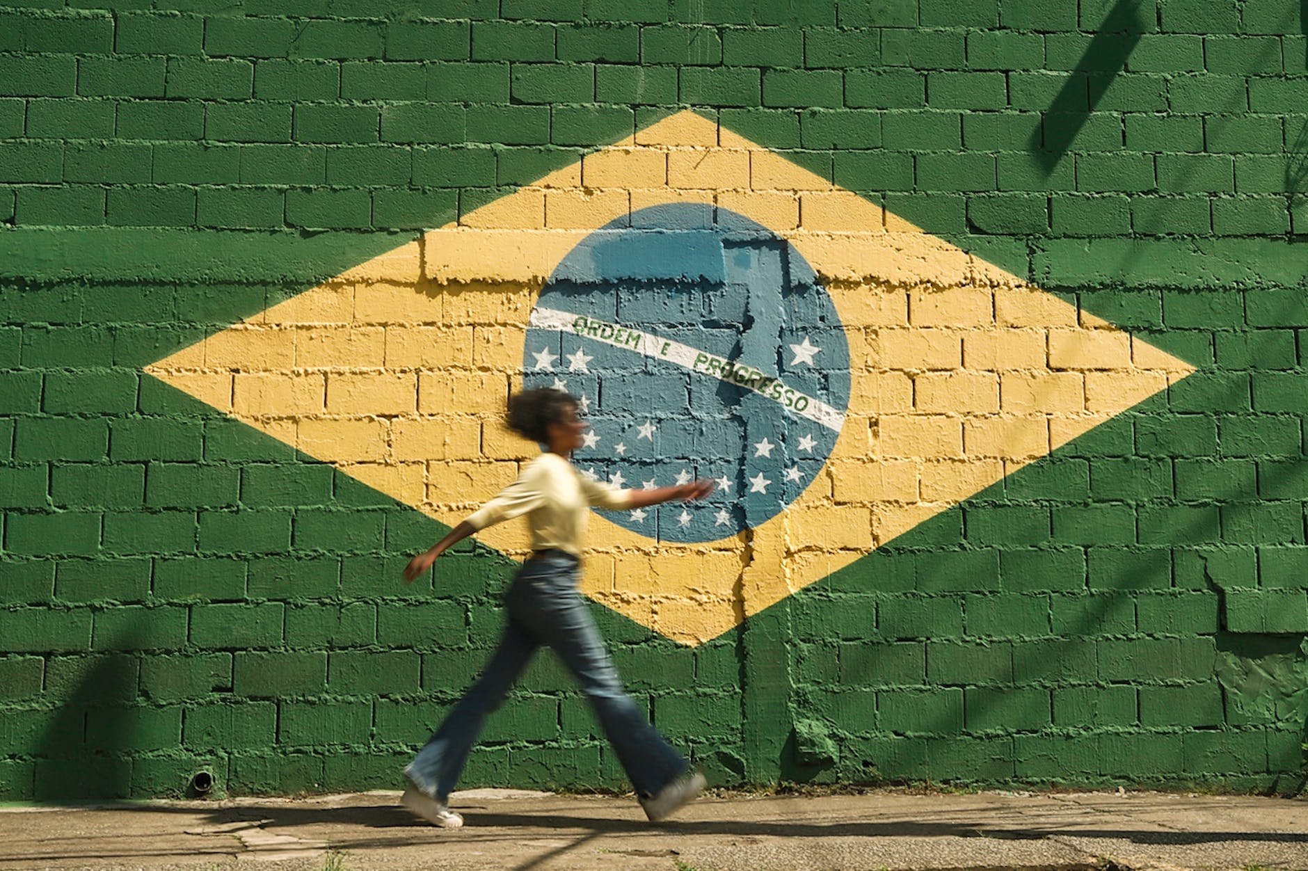bandeira verde amarelo do Brasil , uma mulher negra caminha pela calçada.